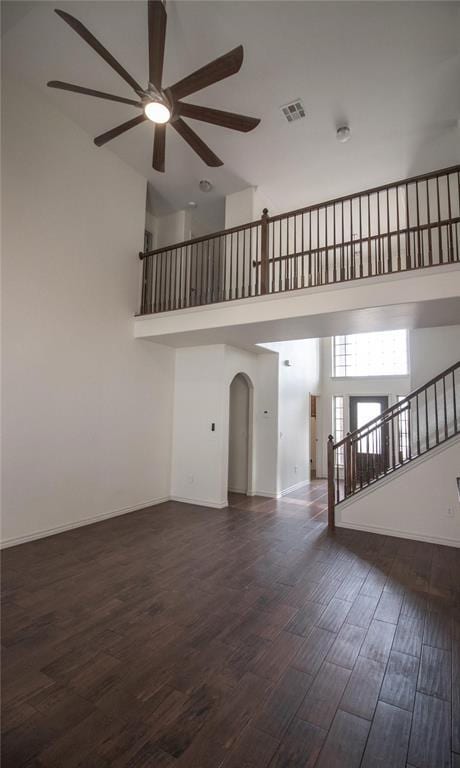 unfurnished living room featuring dark wood-type flooring, ceiling fan, and a high ceiling