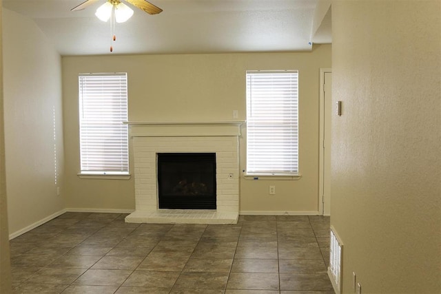 unfurnished living room with ceiling fan, a fireplace, and dark tile patterned flooring