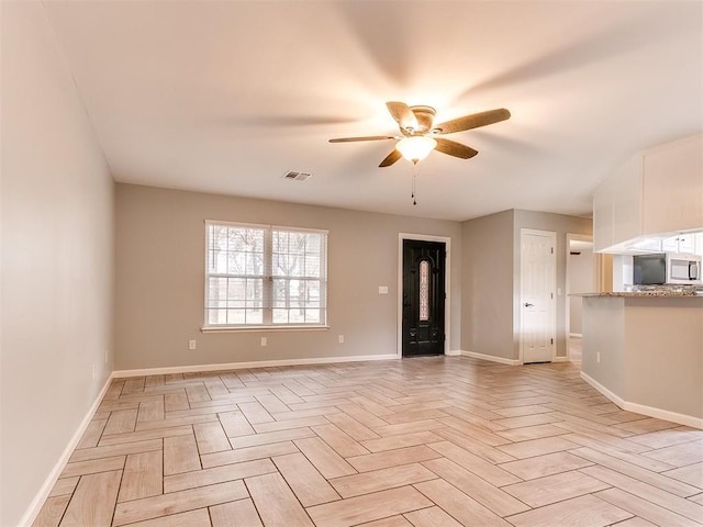 unfurnished living room with visible vents, a ceiling fan, and baseboards
