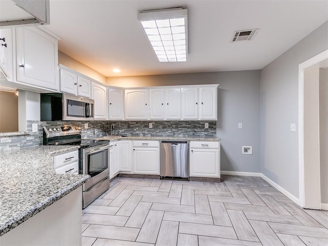 kitchen featuring white cabinets, light stone counters, visible vents, baseboards, and appliances with stainless steel finishes