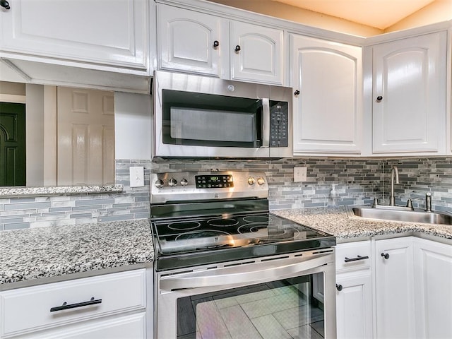 kitchen with white cabinets, stainless steel appliances, a sink, backsplash, and light stone countertops