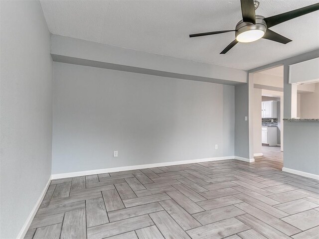 unfurnished room with a textured ceiling, a ceiling fan, and baseboards