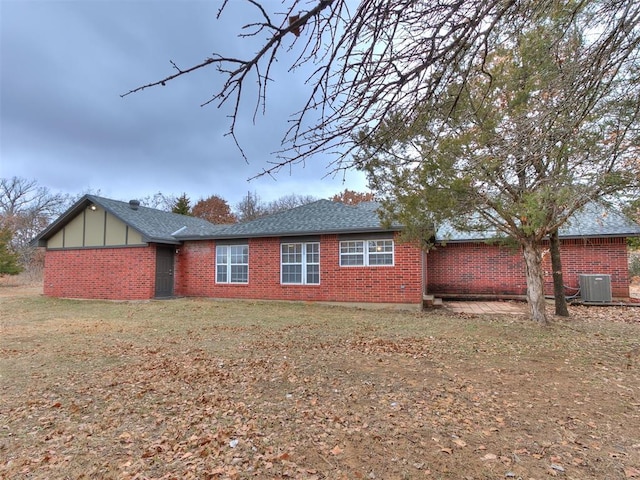 rear view of property with brick siding, cooling unit, and a shingled roof