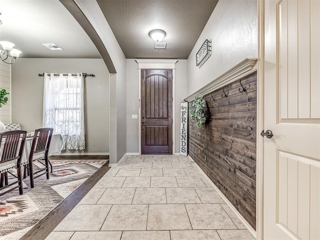 entrance foyer featuring wooden walls, a chandelier, a textured ceiling, and light tile patterned floors