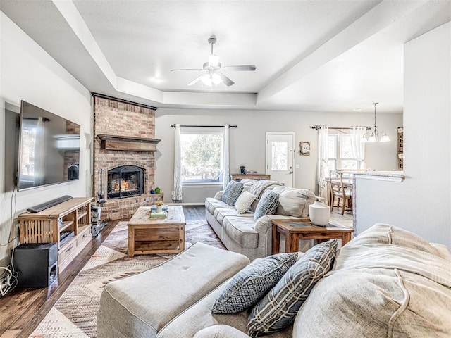 living room featuring a brick fireplace, hardwood / wood-style floors, ceiling fan, and a tray ceiling