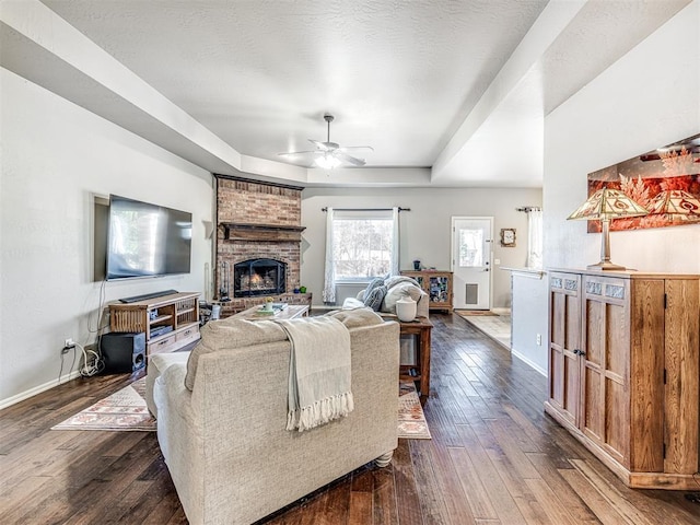 living room with a textured ceiling, dark hardwood / wood-style flooring, a raised ceiling, ceiling fan, and a fireplace