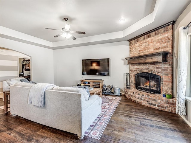 living room with a raised ceiling, ceiling fan, dark wood-type flooring, and a fireplace