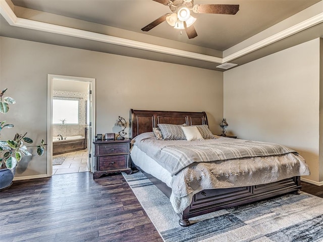 bedroom with dark wood-type flooring, connected bathroom, ceiling fan, and a tray ceiling