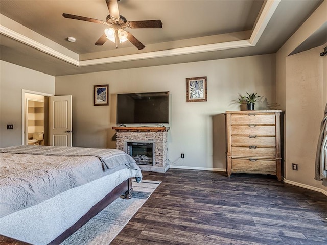 bedroom featuring ceiling fan, dark hardwood / wood-style flooring, a raised ceiling, and a stone fireplace