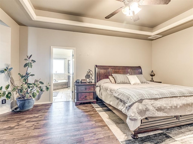 bedroom featuring wood-type flooring, connected bathroom, ceiling fan, and a tray ceiling