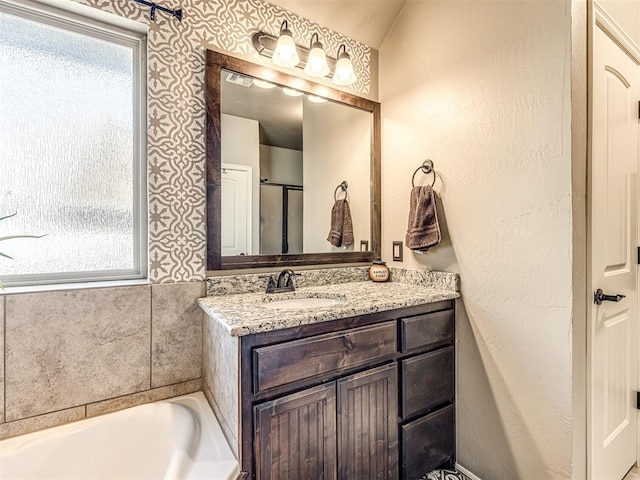 bathroom featuring vanity, a bath, vaulted ceiling, and a healthy amount of sunlight