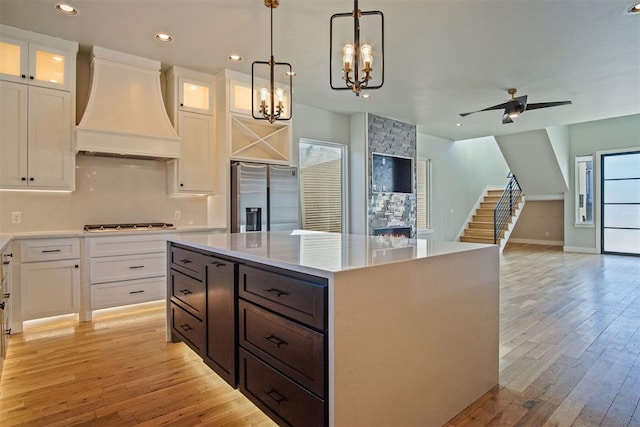 kitchen with a center island, hanging light fixtures, custom range hood, stainless steel appliances, and white cabinets