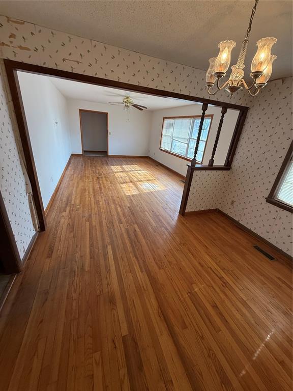 unfurnished living room with ceiling fan with notable chandelier, hardwood / wood-style floors, and a textured ceiling