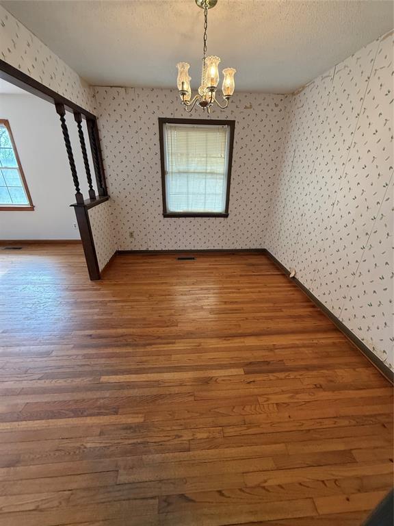 unfurnished dining area featuring hardwood / wood-style flooring, a textured ceiling, and a chandelier