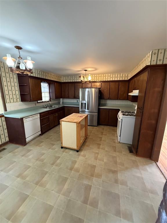 kitchen with pendant lighting, white appliances, an inviting chandelier, butcher block counters, and dark brown cabinetry