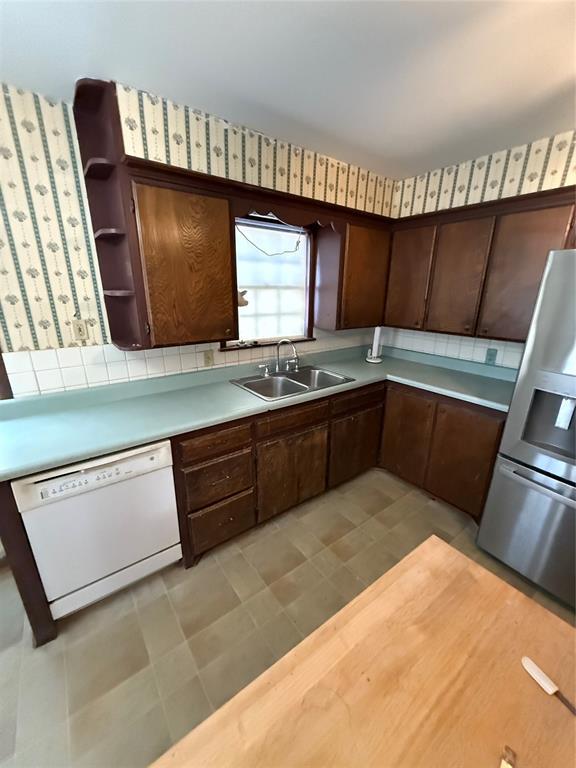 kitchen with stainless steel refrigerator with ice dispenser, dark brown cabinetry, white dishwasher, and sink