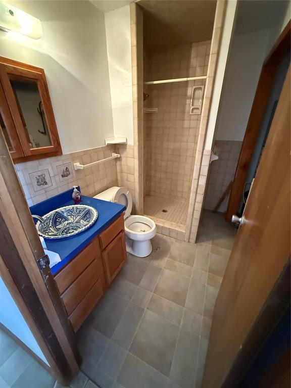 bathroom with tile walls, tiled shower, vanity, tile patterned floors, and toilet