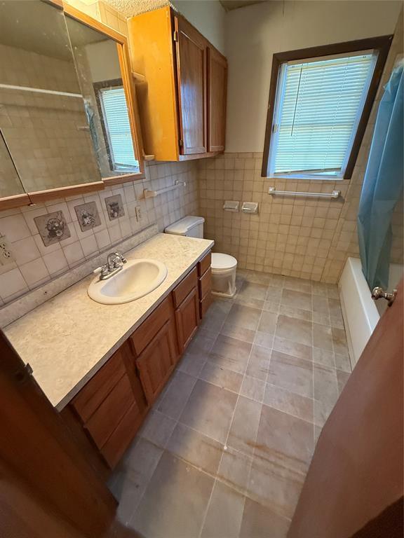 full bathroom with shower / tub combo with curtain, tile walls, tile patterned flooring, vanity, and toilet