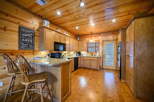 kitchen with decorative light fixtures, black appliances, sink, light stone counters, and kitchen peninsula