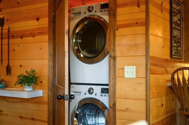 laundry area with stacked washer / drying machine and wooden walls