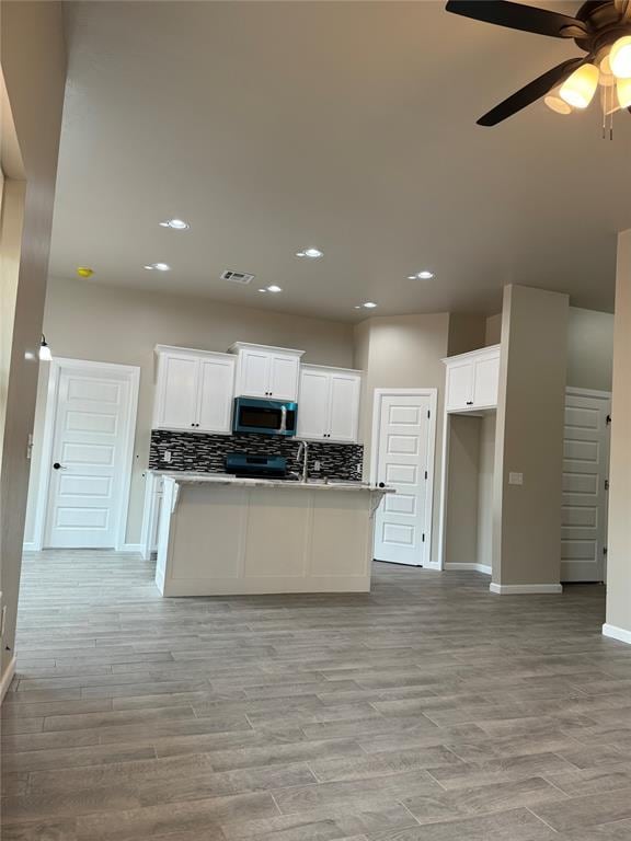 kitchen featuring tasteful backsplash, white cabinetry, sink, ceiling fan, and light wood-type flooring