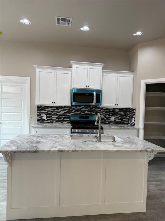 kitchen featuring a center island with sink, light stone countertops, white cabinets, and appliances with stainless steel finishes