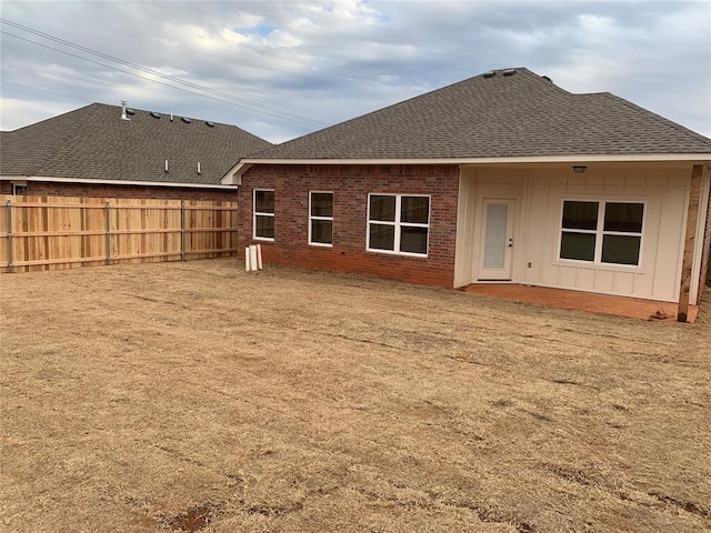 rear view of property with a shingled roof, fence, board and batten siding, and brick siding