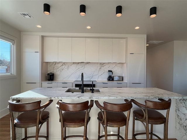 kitchen featuring white cabinetry, sink, and an island with sink