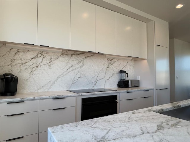 kitchen featuring light stone counters, white cabinetry, decorative backsplash, and black appliances