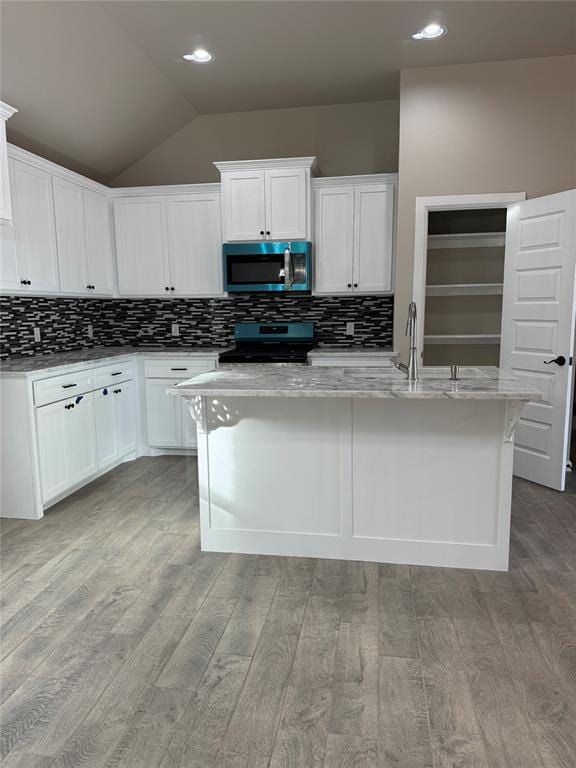 kitchen with an island with sink, lofted ceiling, white cabinets, electric range, and light stone counters