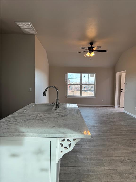 kitchen featuring sink, light stone counters, wood-type flooring, vaulted ceiling, and ceiling fan