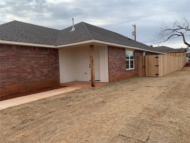 view of side of home with brick siding, fence, and roof with shingles