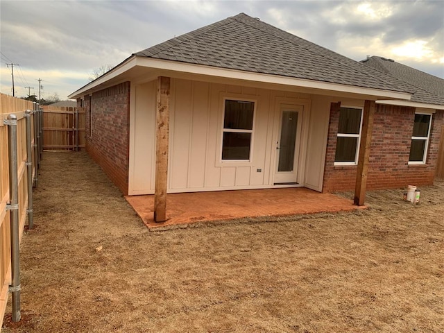 back of property featuring a patio area, roof with shingles, fence, and brick siding