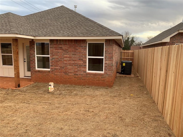 view of home's exterior with a shingled roof, a fenced backyard, brick siding, and central AC unit