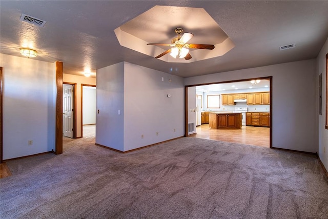 unfurnished living room with ceiling fan, a raised ceiling, and light carpet