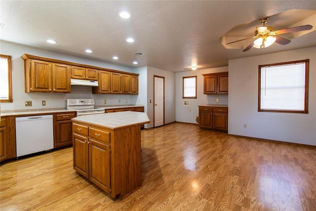 kitchen with a center island, tile counters, ceiling fan, white appliances, and light hardwood / wood-style flooring