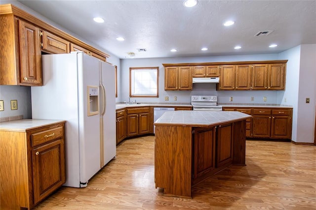 kitchen featuring sink, white appliances, light hardwood / wood-style flooring, a center island, and tile countertops