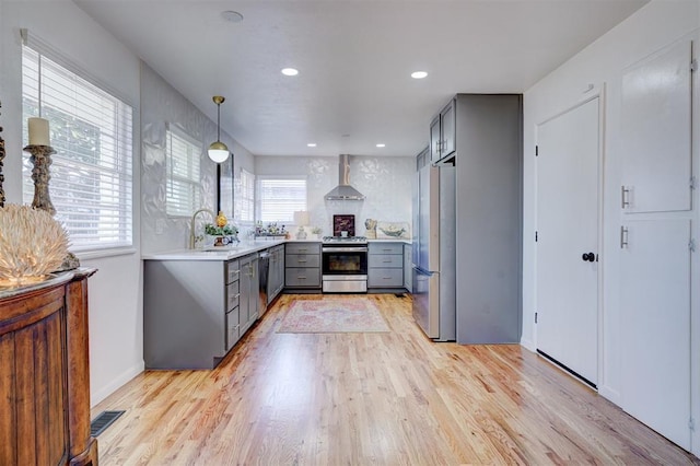 kitchen with gray cabinets, sink, light hardwood / wood-style floors, stainless steel appliances, and wall chimney range hood