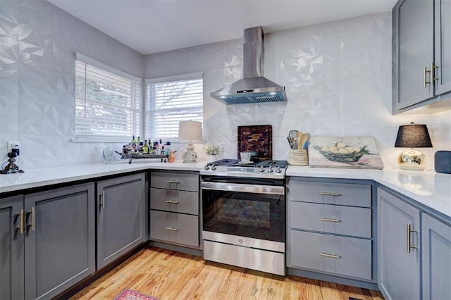 kitchen featuring gray cabinetry, gas range, light hardwood / wood-style flooring, and wall chimney exhaust hood