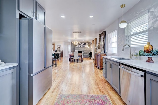 kitchen featuring sink, hanging light fixtures, light hardwood / wood-style flooring, gray cabinets, and stainless steel appliances