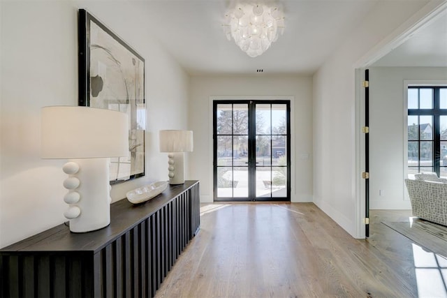 foyer with an inviting chandelier, light hardwood / wood-style flooring, and french doors