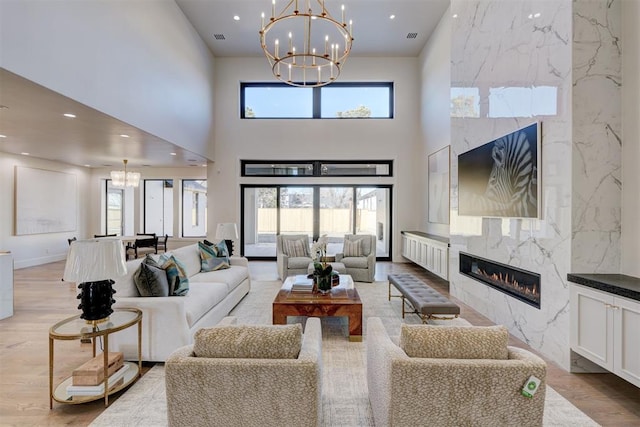 living room featuring a notable chandelier, a high end fireplace, a high ceiling, and light wood-type flooring