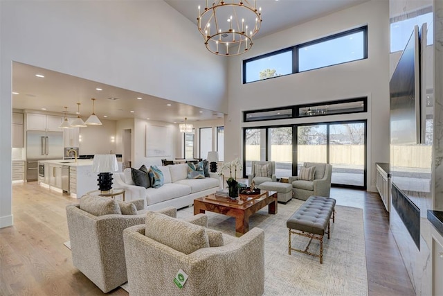 living room with an inviting chandelier, a towering ceiling, and light hardwood / wood-style flooring