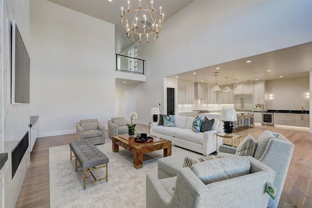 living room with a notable chandelier, light hardwood / wood-style flooring, beverage cooler, and a high ceiling