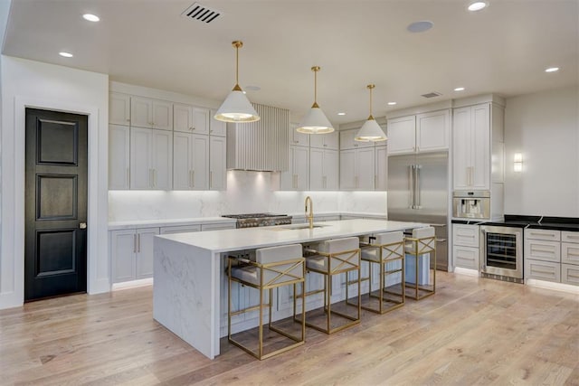 kitchen featuring hanging light fixtures, beverage cooler, white cabinets, and a center island with sink