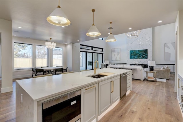 kitchen with sink, decorative light fixtures, an island with sink, light hardwood / wood-style floors, and white cabinets