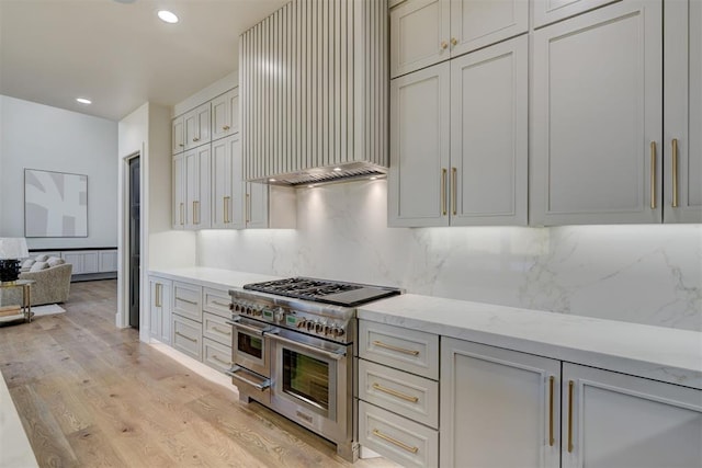 kitchen with light hardwood / wood-style flooring, backsplash, range with two ovens, light stone countertops, and wall chimney exhaust hood