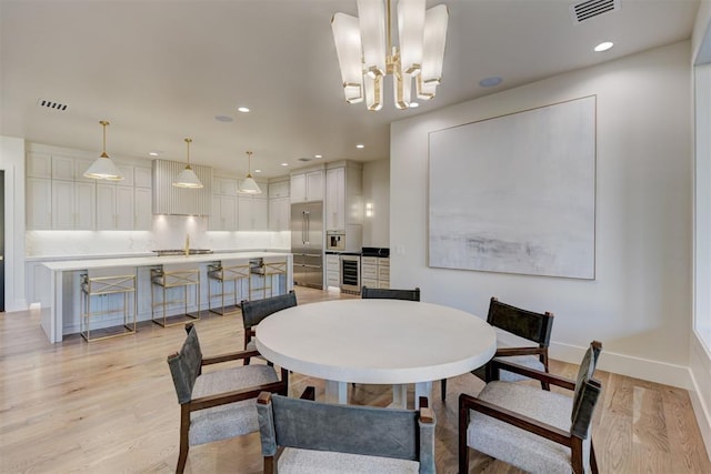 dining room with wine cooler, an inviting chandelier, and light hardwood / wood-style floors