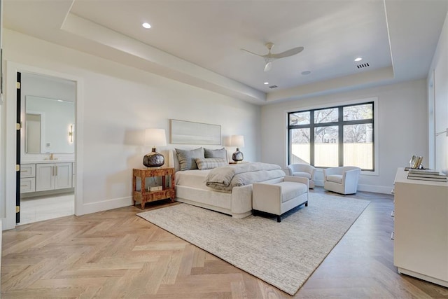 bedroom with ceiling fan, a tray ceiling, ensuite bath, and light parquet flooring