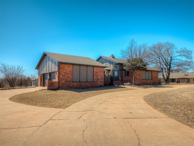 view of front facade with brick siding, a chimney, an attached garage, board and batten siding, and driveway